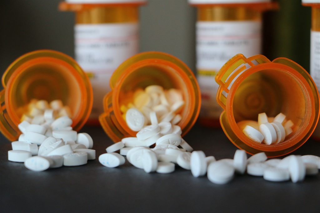 Prescription Drugs: White pills spilling out of prescription bottles with prescriptions in back.